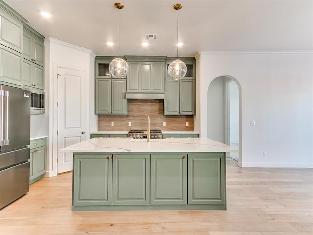 kitchen with hanging light fixtures, stainless steel appliances, green cabinets, an island with sink, and ornamental molding