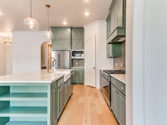 kitchen with a kitchen island with sink, premium appliances, light stone countertops, decorative light fixtures, and light wood-type flooring