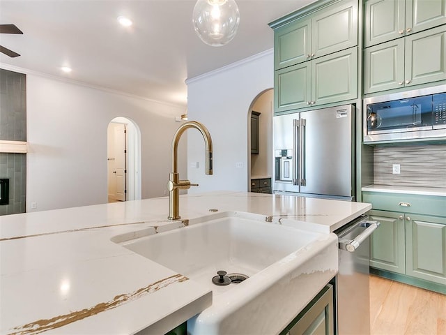 kitchen featuring sink, appliances with stainless steel finishes, ornamental molding, green cabinetry, and light wood-type flooring