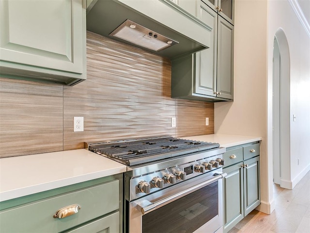 kitchen with high end range, backsplash, custom exhaust hood, and light hardwood / wood-style flooring