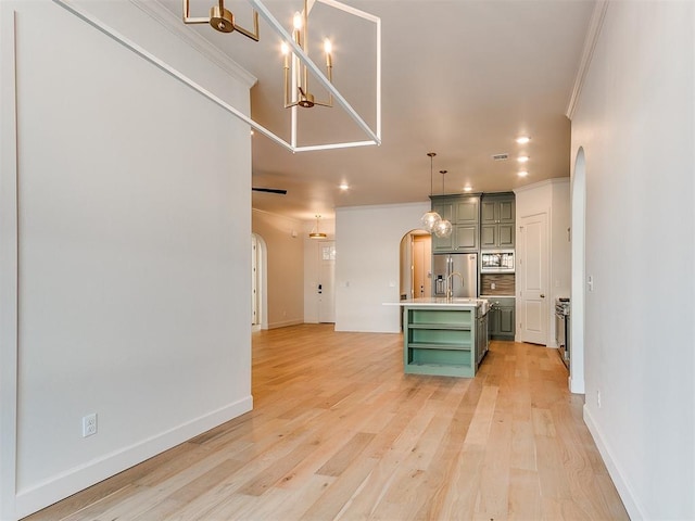 kitchen featuring crown molding, appliances with stainless steel finishes, green cabinetry, a center island with sink, and light wood-type flooring