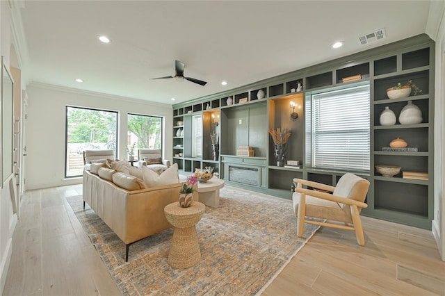 living room with ceiling fan, light hardwood / wood-style floors, built in features, and crown molding