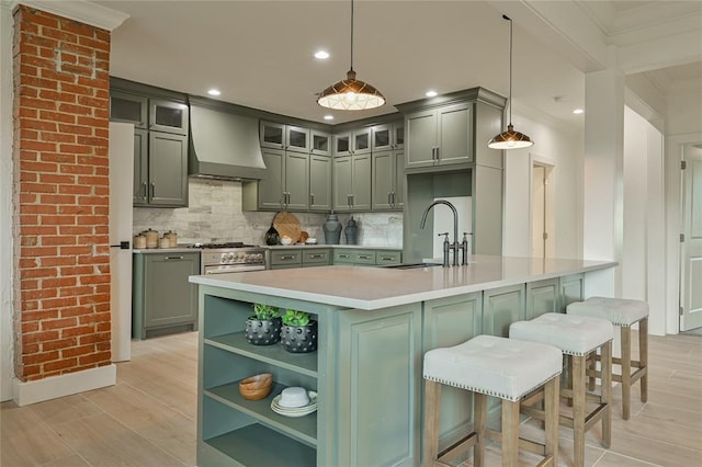 kitchen featuring sink, wall chimney range hood, backsplash, high end stove, and decorative light fixtures