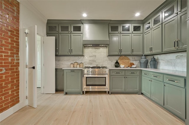 kitchen with high end range, green cabinets, decorative backsplash, and wall chimney exhaust hood