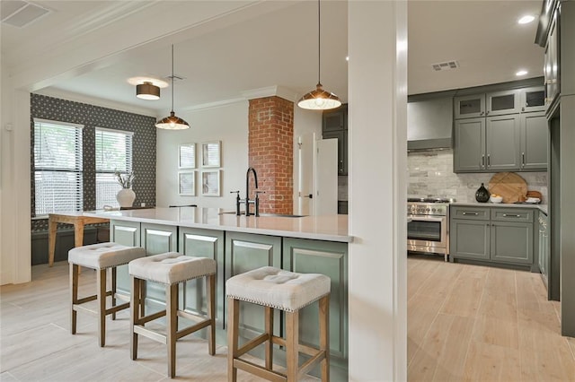 kitchen with hanging light fixtures, wall chimney range hood, sink, and high end stainless steel range