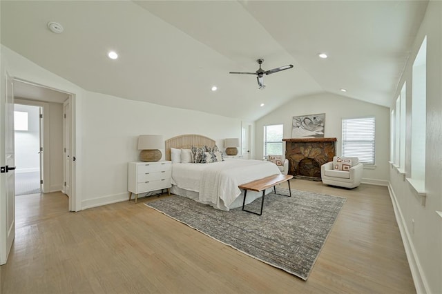 bedroom with a stone fireplace, ceiling fan, vaulted ceiling, and light wood-type flooring