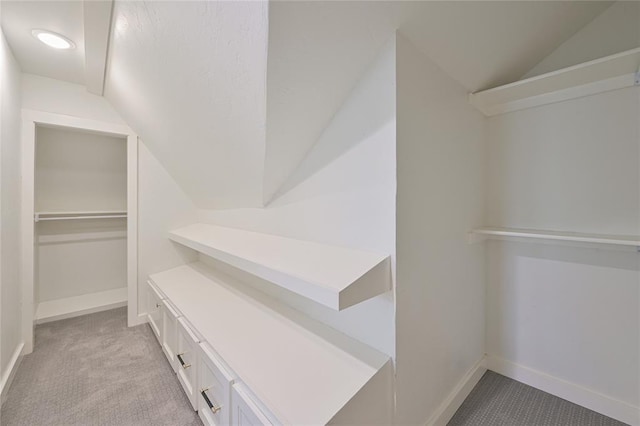 walk in closet with light colored carpet and lofted ceiling