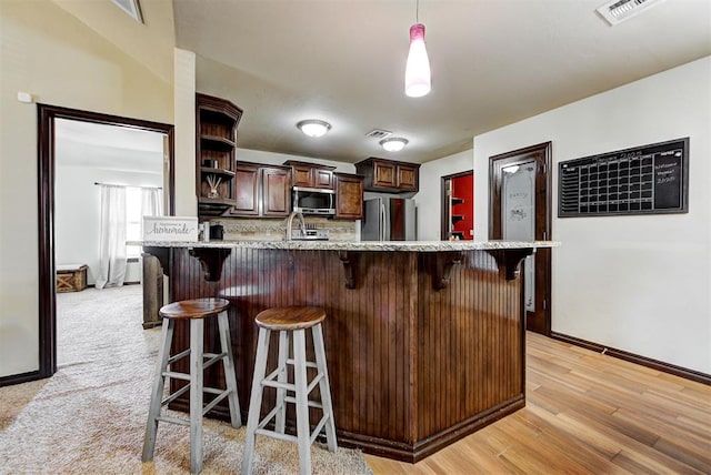 kitchen with a breakfast bar area, appliances with stainless steel finishes, light hardwood / wood-style floors, dark brown cabinets, and decorative light fixtures