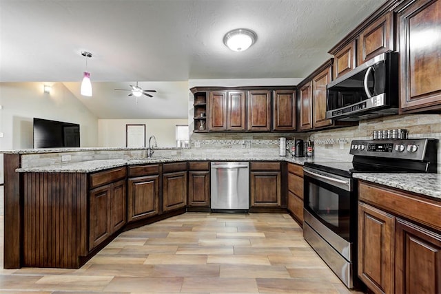 kitchen featuring stainless steel appliances, kitchen peninsula, light stone countertops, sink, and tasteful backsplash