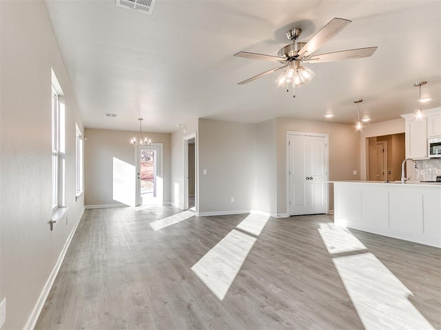 unfurnished living room featuring sink, light wood-type flooring, and ceiling fan with notable chandelier