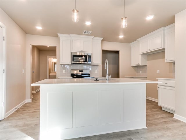 kitchen featuring decorative light fixtures, stainless steel appliances, a center island with sink, and white cabinetry