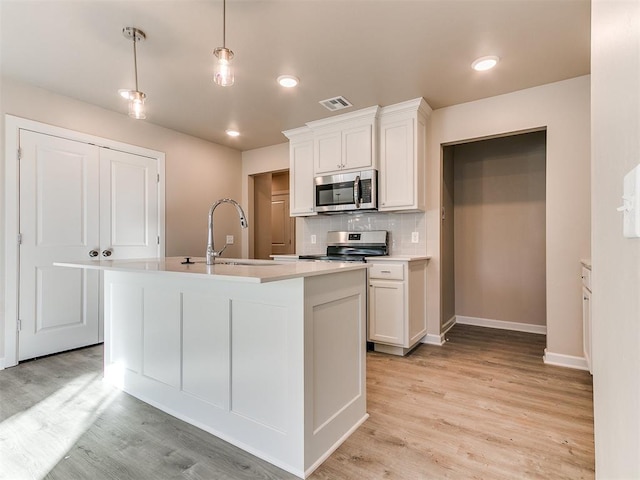 kitchen featuring a center island with sink, appliances with stainless steel finishes, pendant lighting, sink, and white cabinetry