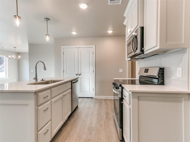 kitchen featuring sink, stainless steel appliances, a kitchen island with sink, and hanging light fixtures