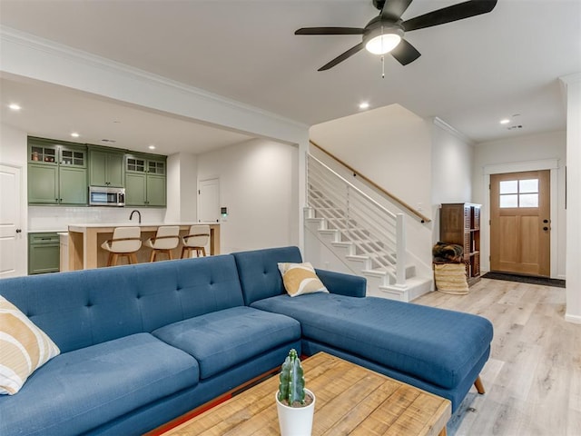 living room with ceiling fan, sink, ornamental molding, and light hardwood / wood-style flooring