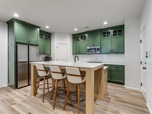 kitchen featuring light wood-type flooring, green cabinets, appliances with stainless steel finishes, and a kitchen island with sink