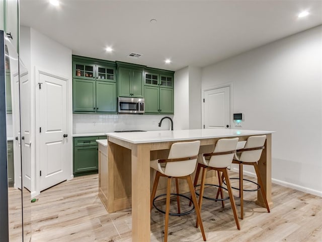 kitchen with an island with sink, backsplash, green cabinets, and light hardwood / wood-style floors