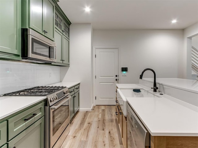 kitchen with appliances with stainless steel finishes, decorative backsplash, sink, light hardwood / wood-style floors, and green cabinets