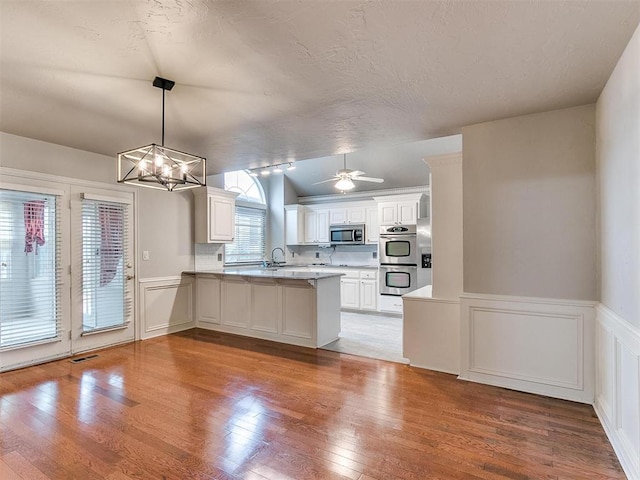 kitchen with appliances with stainless steel finishes, decorative light fixtures, white cabinetry, sink, and kitchen peninsula