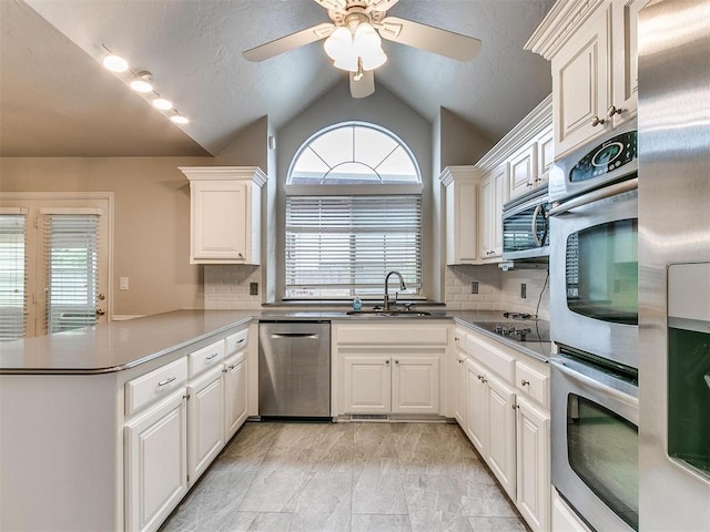 kitchen featuring vaulted ceiling, appliances with stainless steel finishes, sink, white cabinets, and kitchen peninsula