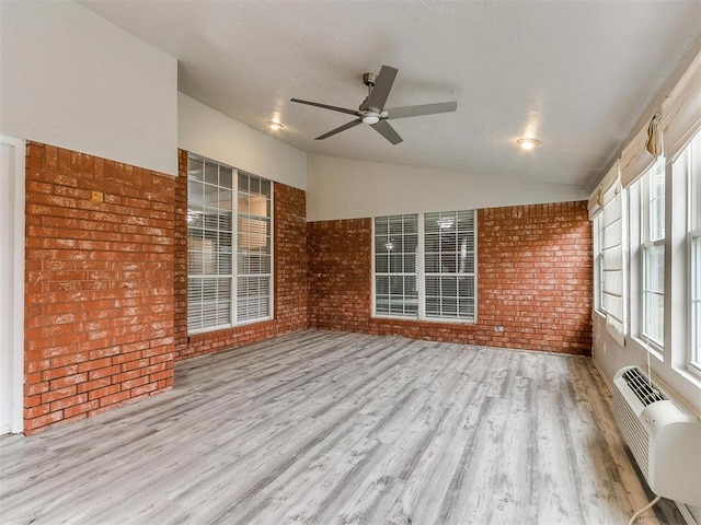 interior space featuring vaulted ceiling, brick wall, an AC wall unit, ceiling fan, and light wood-type flooring