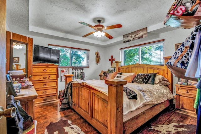 bedroom with ceiling fan, dark hardwood / wood-style flooring, a raised ceiling, and wooden walls