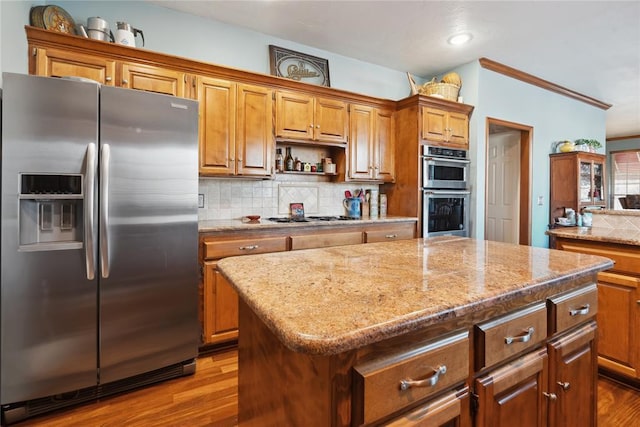 kitchen featuring a center island, backsplash, light wood-type flooring, appliances with stainless steel finishes, and ornamental molding