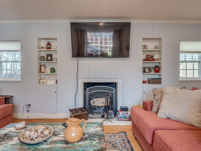 living room featuring built in shelves, ornamental molding, hardwood / wood-style flooring, and a fireplace