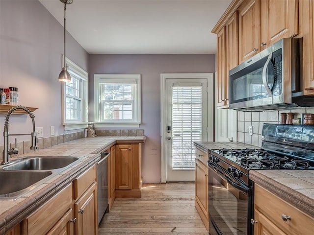 kitchen with stainless steel appliances, light wood-type flooring, hanging light fixtures, tile countertops, and sink