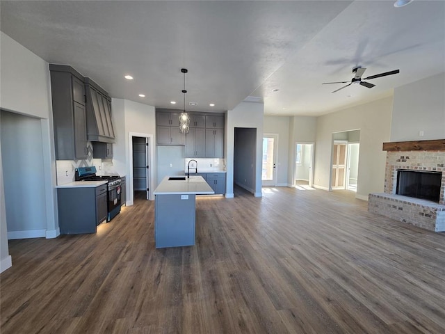 kitchen with pendant lighting, custom exhaust hood, stainless steel range with gas cooktop, a kitchen island with sink, and dark wood-type flooring