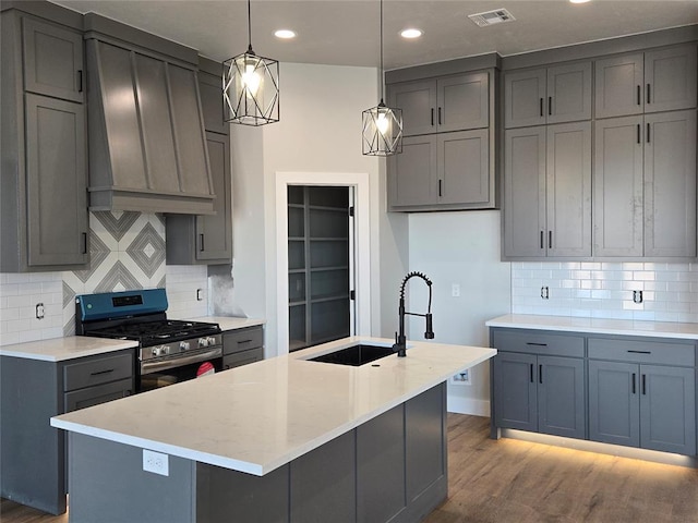 kitchen featuring stainless steel range with gas cooktop, hanging light fixtures, gray cabinets, and an island with sink