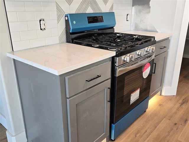 kitchen featuring gray cabinetry, light hardwood / wood-style flooring, tasteful backsplash, and stainless steel gas range oven