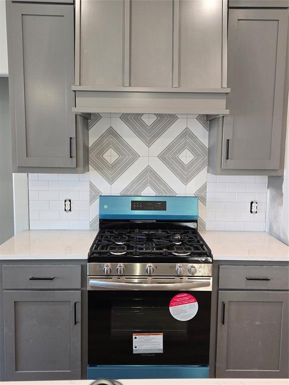 kitchen featuring decorative backsplash, stainless steel gas range oven, and gray cabinetry