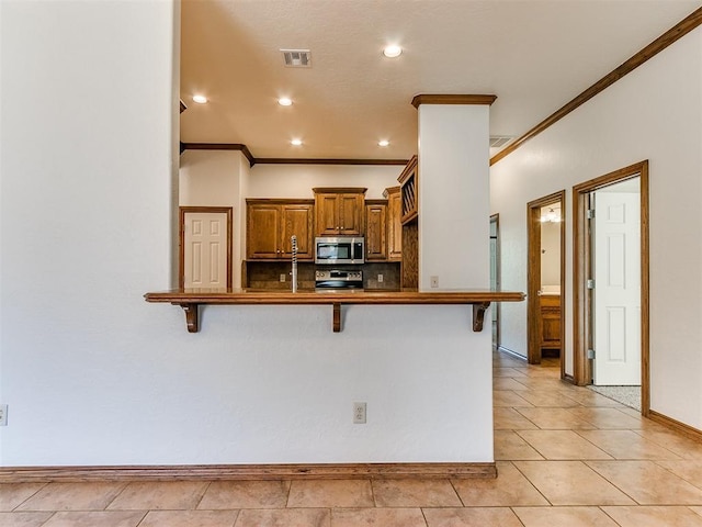 kitchen with appliances with stainless steel finishes, a breakfast bar, ornamental molding, and kitchen peninsula