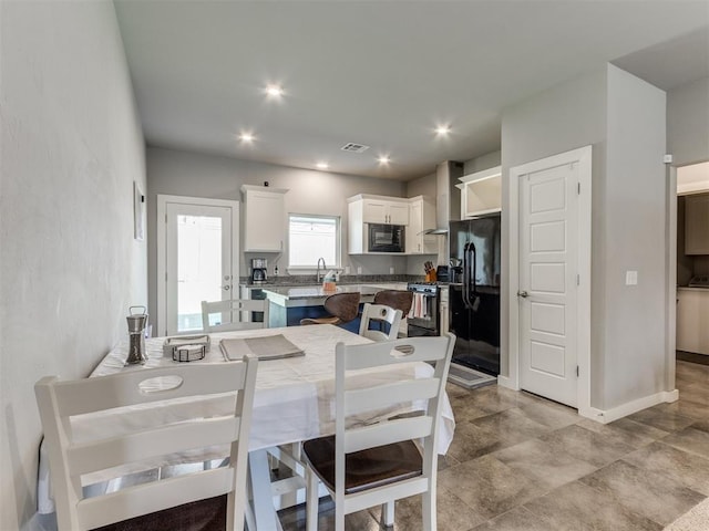 kitchen featuring black appliances, light stone counters, a kitchen island, wall chimney exhaust hood, and white cabinetry