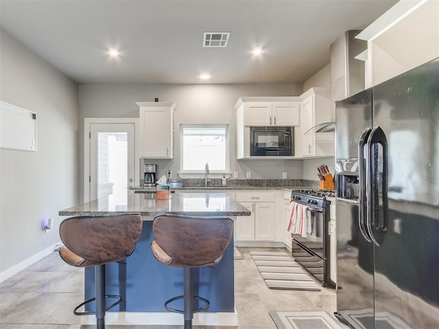 kitchen with black appliances, white cabinetry, dark stone countertops, and a kitchen island