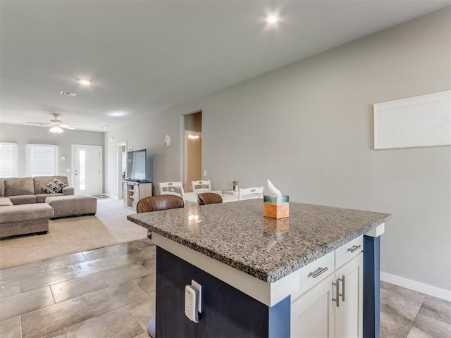 kitchen with white cabinets, ceiling fan, stone counters, and a kitchen island