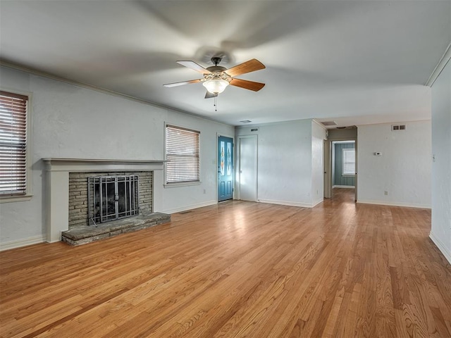 unfurnished living room featuring ceiling fan, crown molding, light wood-type flooring, and a stone fireplace