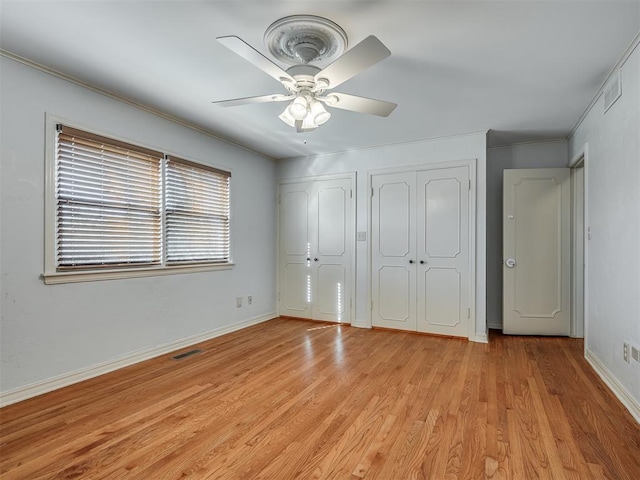 unfurnished bedroom with two closets, ceiling fan, ornamental molding, and light hardwood / wood-style flooring