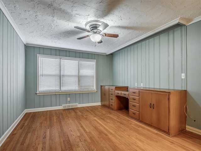 unfurnished office with wood walls, ceiling fan, ornamental molding, and light hardwood / wood-style floors