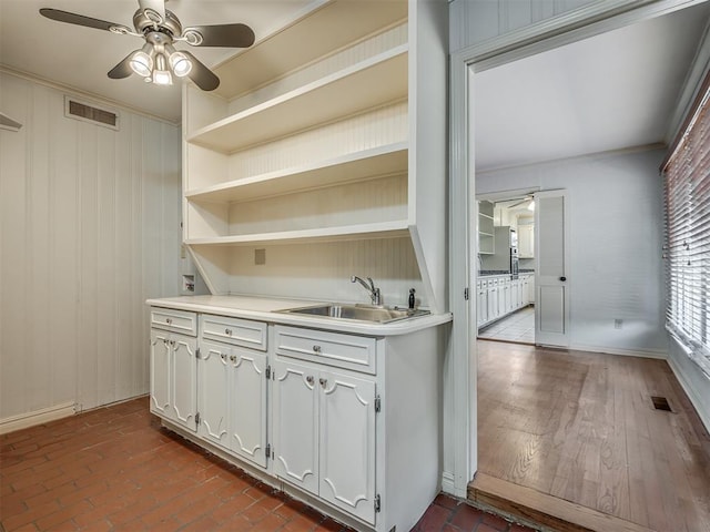 interior space featuring wood walls, crown molding, white cabinets, ceiling fan, and sink