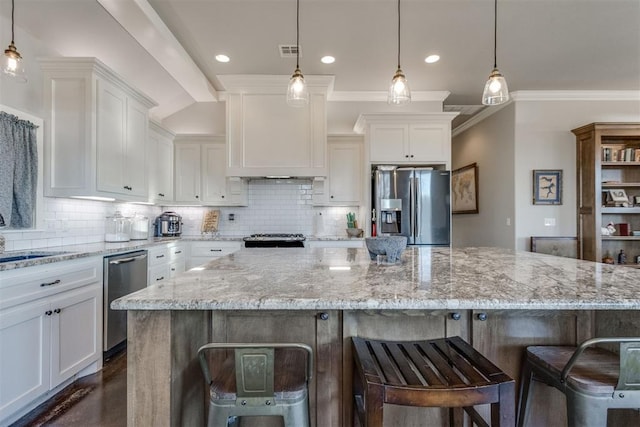 kitchen featuring stainless steel appliances, white cabinets, a kitchen bar, a spacious island, and pendant lighting