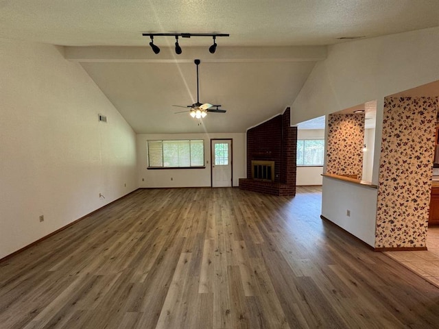 unfurnished living room with ceiling fan, a fireplace, hardwood / wood-style floors, and vaulted ceiling with beams