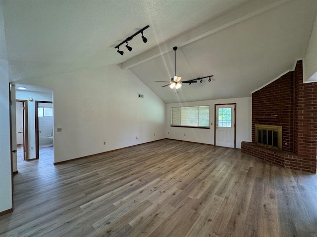 unfurnished living room with rail lighting, light wood-type flooring, lofted ceiling with beams, ceiling fan, and a brick fireplace