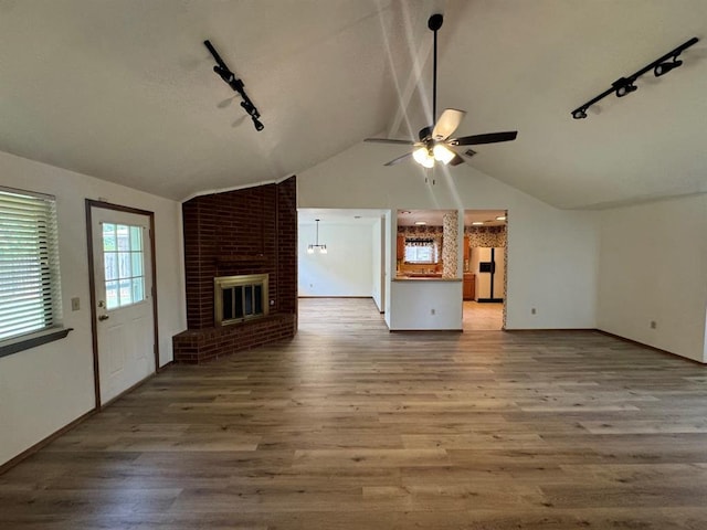 unfurnished living room with a fireplace, vaulted ceiling, ceiling fan, hardwood / wood-style flooring, and track lighting