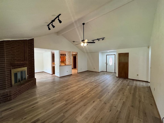 unfurnished living room featuring a fireplace, ceiling fan, hardwood / wood-style flooring, rail lighting, and lofted ceiling with beams