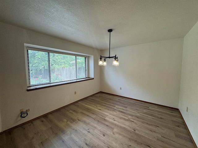 unfurnished dining area featuring an inviting chandelier, a textured ceiling, and hardwood / wood-style floors