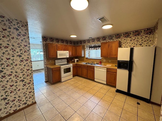 kitchen featuring white appliances, a textured ceiling, light tile patterned floors, and sink