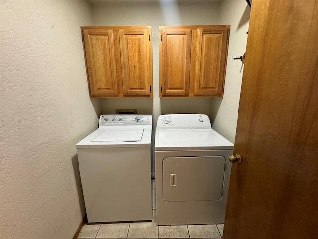 washroom with light tile patterned flooring, washing machine and clothes dryer, and cabinets