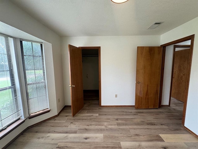 unfurnished bedroom with a walk in closet, a closet, and light hardwood / wood-style flooring