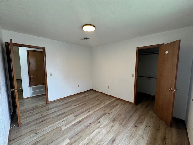 unfurnished bedroom with a walk in closet, a closet, and light hardwood / wood-style flooring